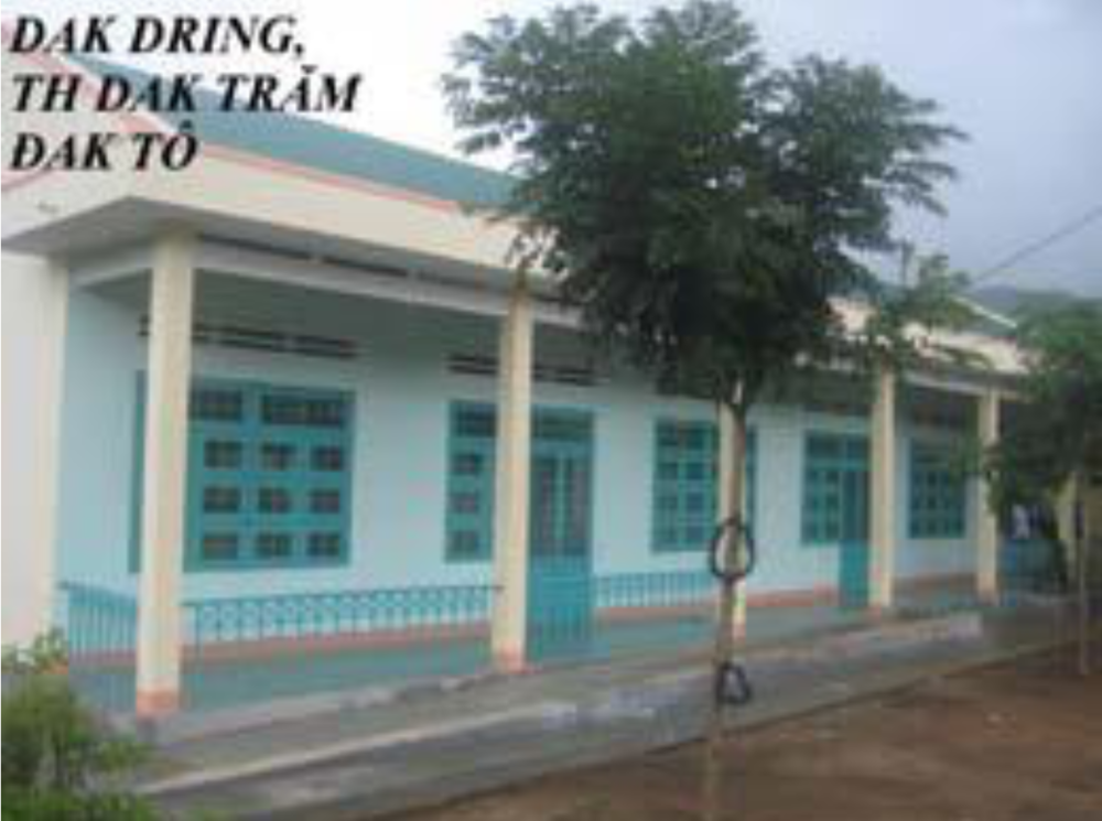 A single-story building with teal doors and windows, a covered walkway supported by pillars, and trees in front. Text in the top left corner reads: "DAK DRING, TH DAK TRÄ‚M ÄAK TÃ”.
