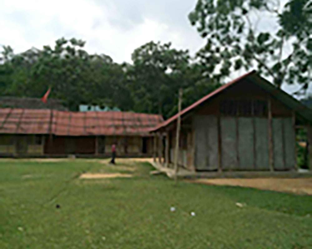 A blurred image of a rural setting with two wooden buildings with red roofs surrounded by greenery. A person is visible between the buildings.