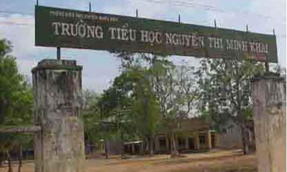 1Entrance gate of Nguyen Thi Minh Khai Elementary School with green sign, white text, and surrounding trees and buildings in the background.